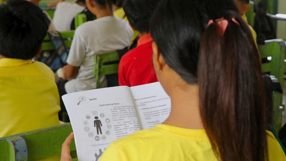 A grade-school girl diligently studies a learning module on the fundamental principles of human rights. © UNFPA Philippines/ Mark Sambajon