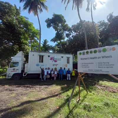 A group of people posing for a photo while in front of the Women’s Health on Wheels mobile birthing unit