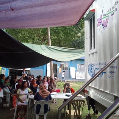 A group of people sitting down beside the Women’s Health on Wheels mobile birthing unit