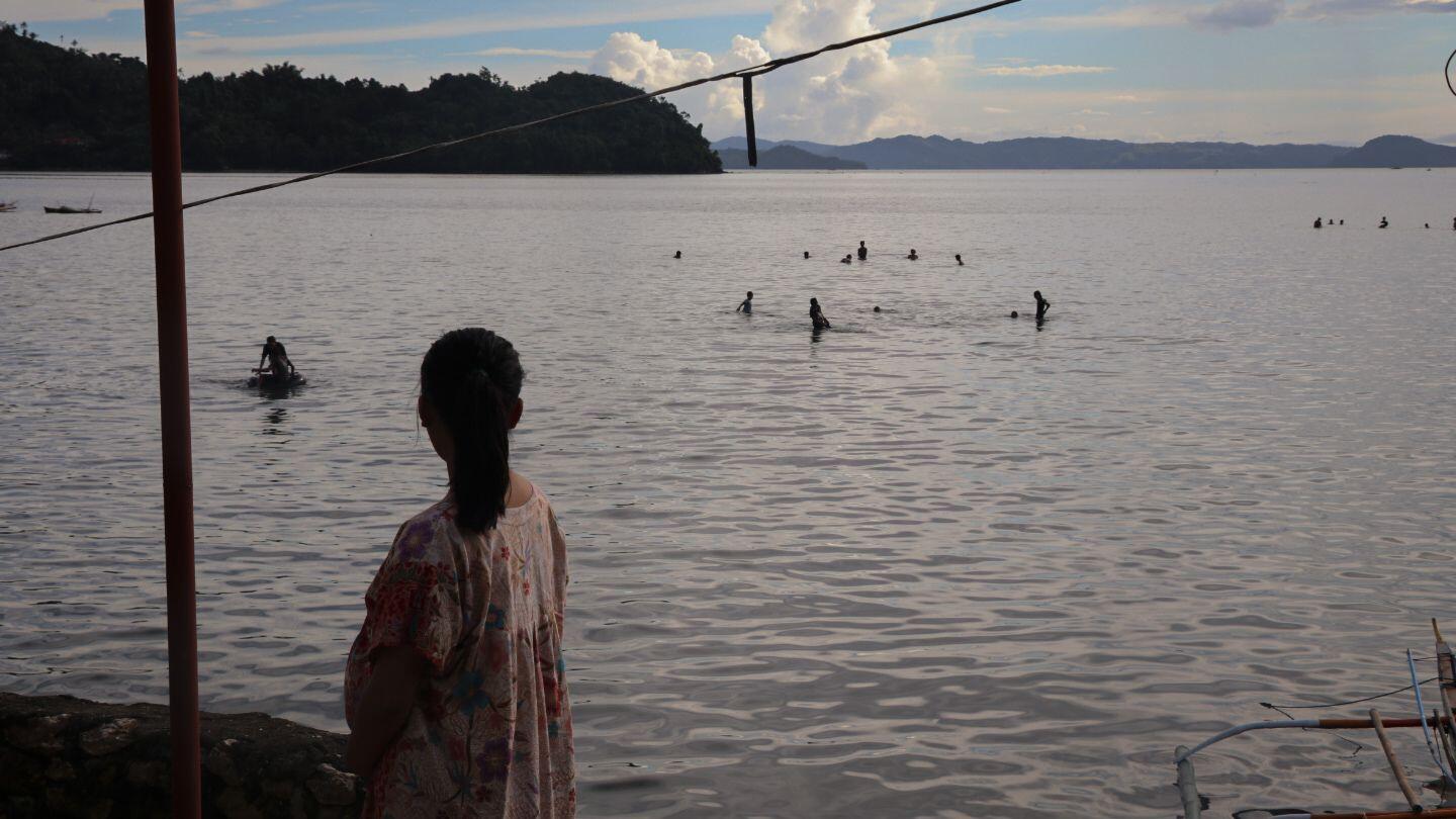 A pregnant teenage girl watches young people swimming along the shore. © UNFPA Philippines/Mark Sambajon