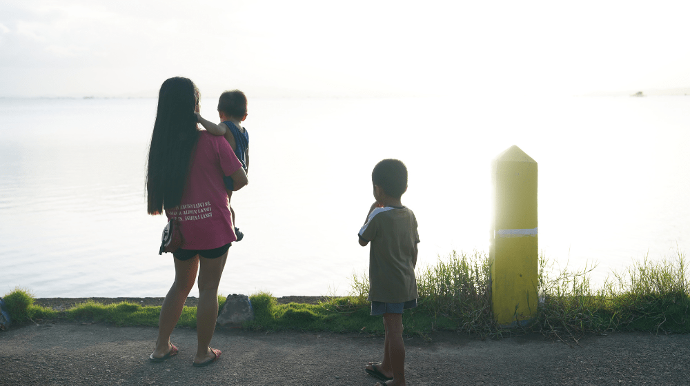 Young woman carrying a child while another child looks on.